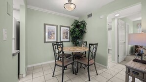 Un coin repas avec une table ronde et quatre chaises, une plante en pot et deux tableaux encadrés au mur.