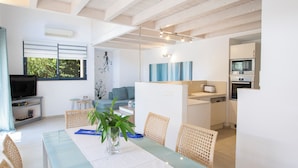 Une cuisine moderne dotée d’appareils électroménagers intégrés, un coin repas avec une table en verre, des chaises en osier et une grande fenêtre.