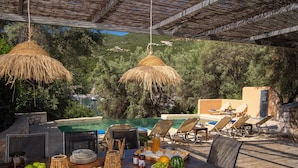 Un espace extérieur aménagé pour les repas, avec une piscine, des chaises longues et une table dressée avec de la nourriture et des boissons.