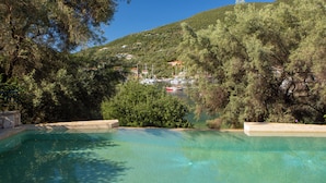 Une piscine aux eaux cristallines, entourée d’arbres, avec vue sur une colline parsemée de bâtiments.