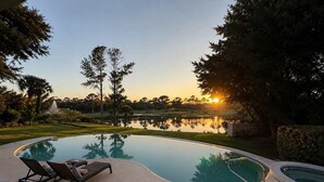Ein Schwimmbad mit Liegestühlen, einem kleinen Wasserspiel und Blick auf einen Golfplatz bei Sonnenuntergang.