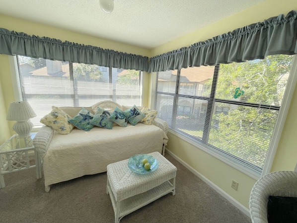 Un dormitorio con cama, una mesita, una lámpara y ventanas amplias con persianas.