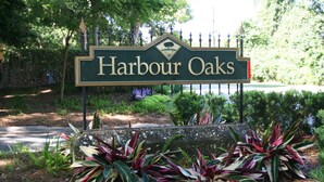 Schild für Harbour Oaks mit dekorativem Zaun und angelegten Pflanzen.