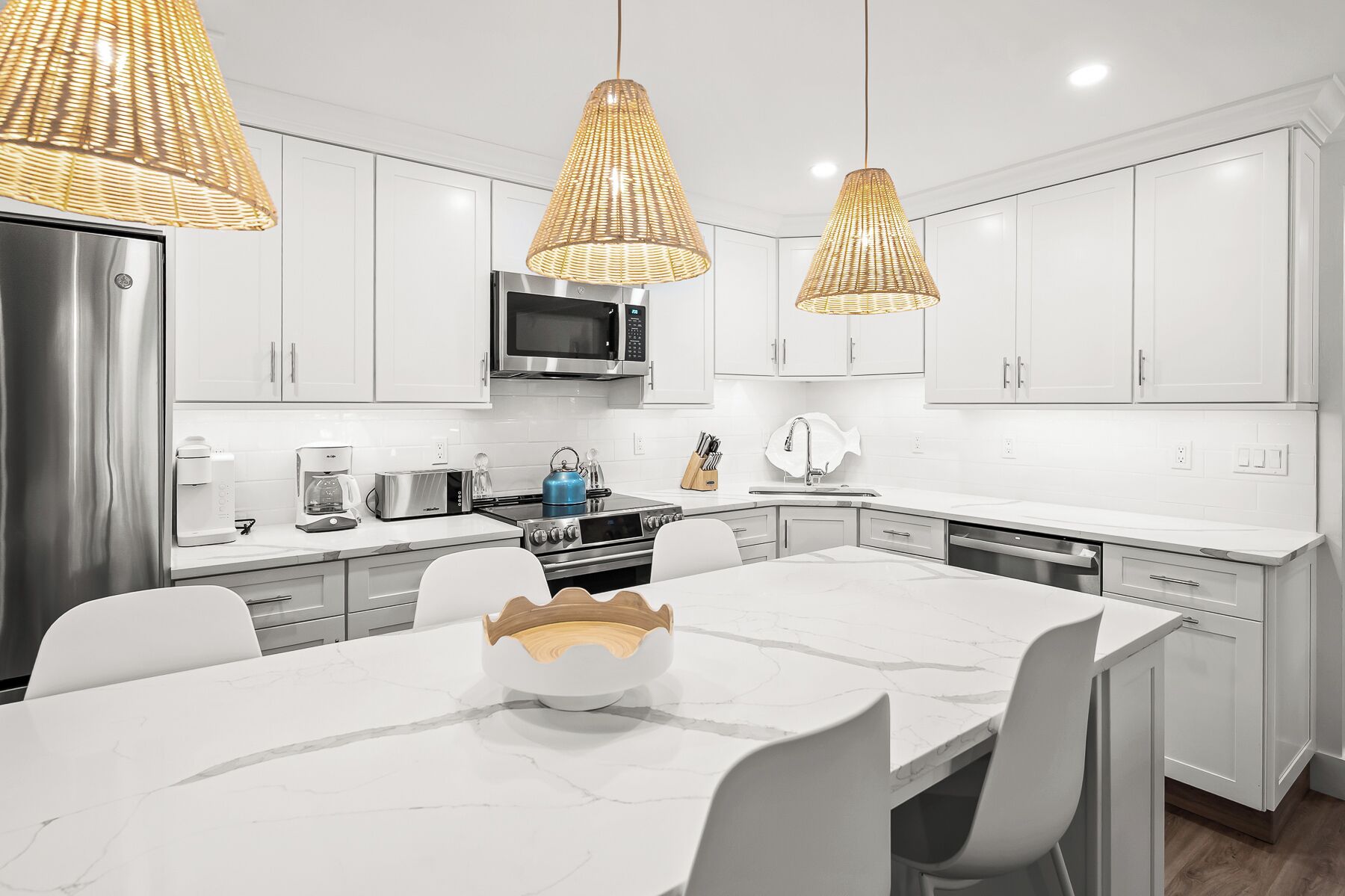 A modern kitchen with white cabinetry, stainless steel appliances, and a marble countertop.