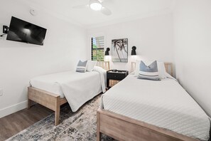 Une chambre avec deux lits, une télévision, un ventilateur de plafond et une fenêtre avec des stores.