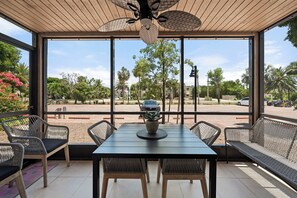 Une terrasse couverte avec une table et des chaises, de grandes fenêtres et un ventilateur de plafond.
