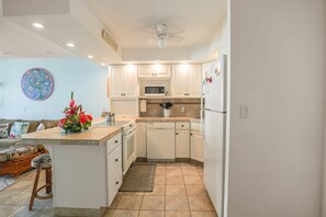 A compact kitchen with white cabinetry, a microwave, a dishwasher, and a ceiling fan.