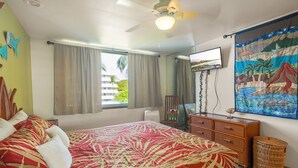 Une chambre à coucher avec un lit, un ventilateur de plafond, une télévision, un tableau et une fenêtre avec des rideaux.