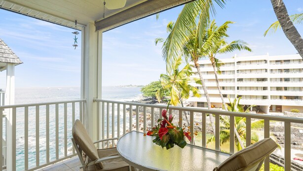 Un balcon avec une table et des chaises, donnant sur une plage et l’océan.