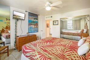Un dormitorio con cama, televisor, ventilador de techo y un espejo grande.