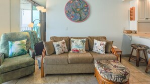 Un salon avec un canapé, des fauteuils et une table basse. Un tableau est accroché au mur et une fenêtre offre une vue agréable.