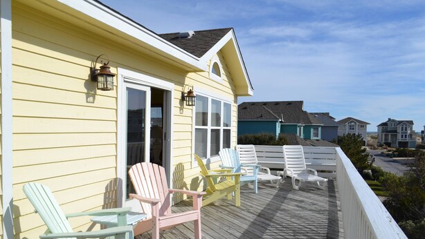 A wooden deck with Adirondack chairs and a covered area with a door and windows.