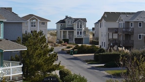 A residential street with houses, a stop sign, and a green trash bin.