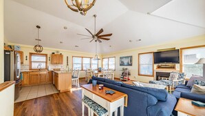 A spacious living area with a wooden dining table, blue sofa, and a television mounted on the wall.