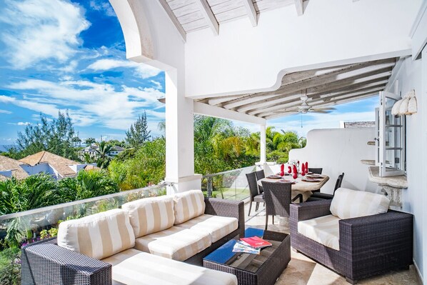 A covered outdoor seating area with wicker furniture and a view of the surrounding greenery.