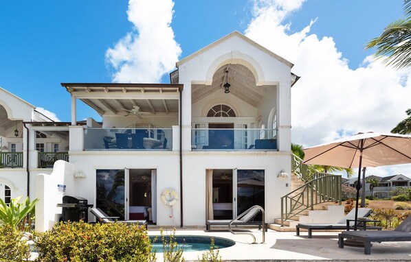 A two-story house with a balcony, a swimming pool, and outdoor seating.