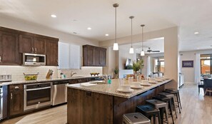A modern kitchen with dark wood cabinets, stainless steel appliances, a large island with bar stools, and pendant lighting. - 98 - Grand Resort in St George with Private Pool and Rec Court (Santa Clara)