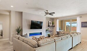 A modern living room with a large sectional sofa, a flat-screen TV, a fireplace, and a ceiling fan. - 98 - Grand Resort in St George with Private Pool and Rec Court (Santa Clara)