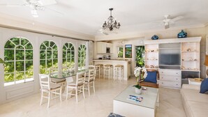 A spacious living area with a dining table, white chairs, a glass coffee table, and a bookshelf. - Enchanting Beachfront Retreat - Leamington Cottage (Battaleys)