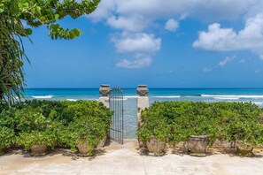 A beach entrance with a gate, lush greenery, and a view of the ocean.