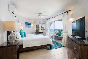 A hotel room with a bed, a TV, a balcony with a view, and a ceiling fan. - Modern Beachfront Condo with Pool - Sapphire 317 (Saint Lawrence Gap)