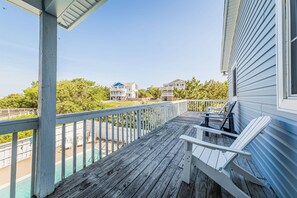 A wooden deck with a railing, a white Adirondack chair, and a view of houses and trees. - The Sailfish - Duck, Carolina Dunes, Beach 300 Yds, Sound View, Pool, Hot Tub, Pets OK, Flex Stays (Duck)
