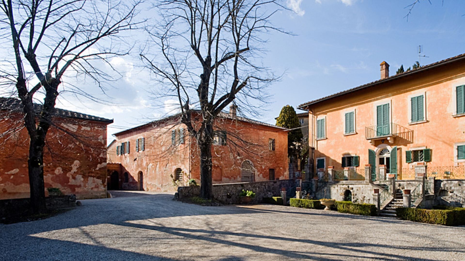 A courtyard with two historic buildings, one with a red facade and the other with a pink facade, both featuring arched windows and a central entrance.