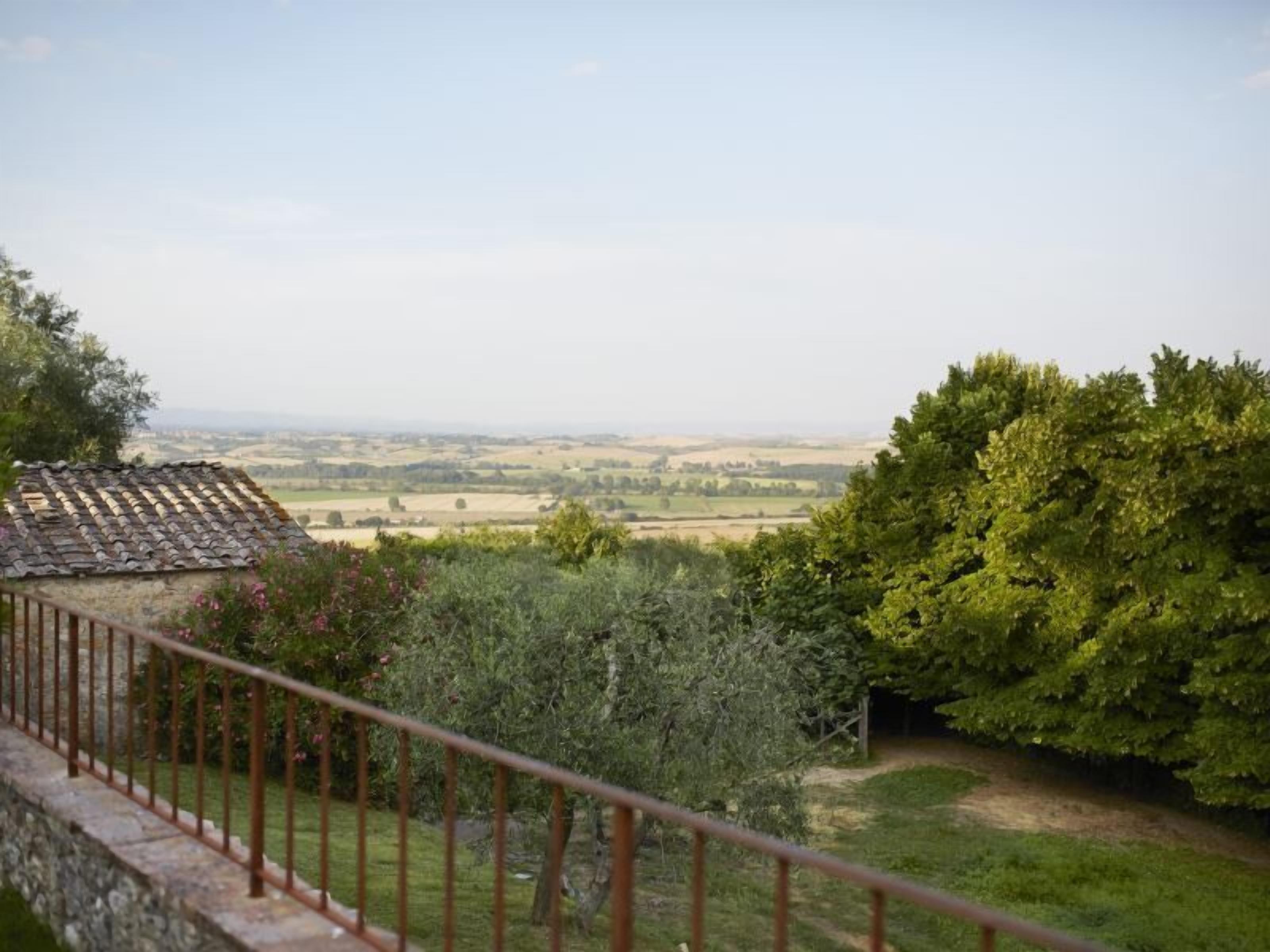 A balcony with a stone balustrade overlooking a rural landscape with fields and trees.