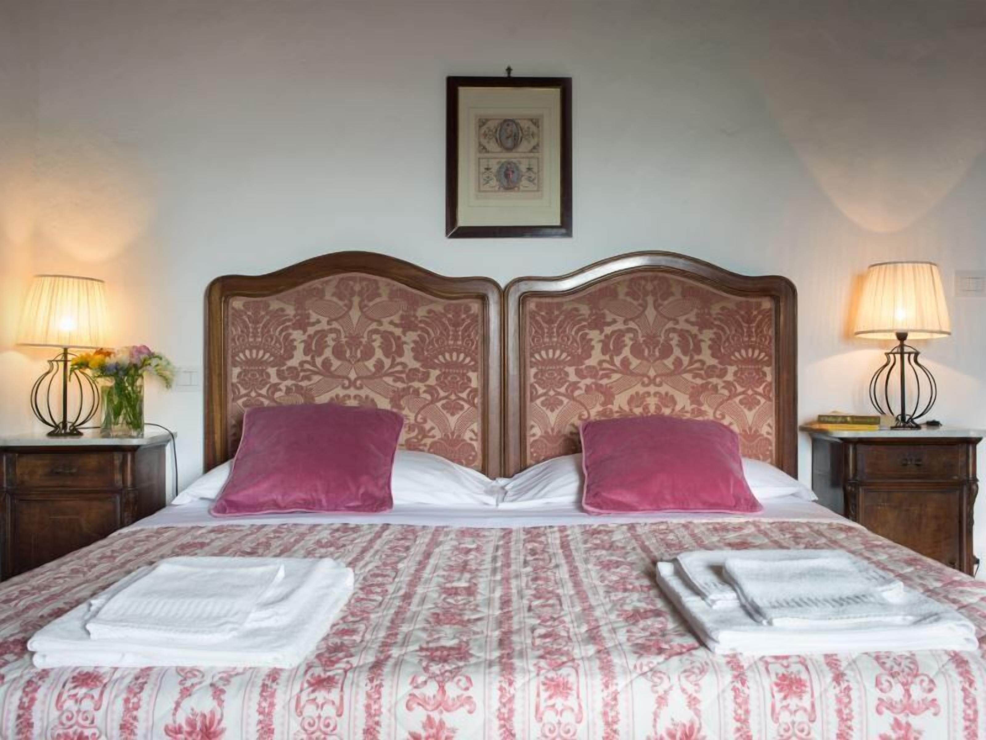 A double bed with a patterned bedspread, two pillows, and two bedside tables with lamps.