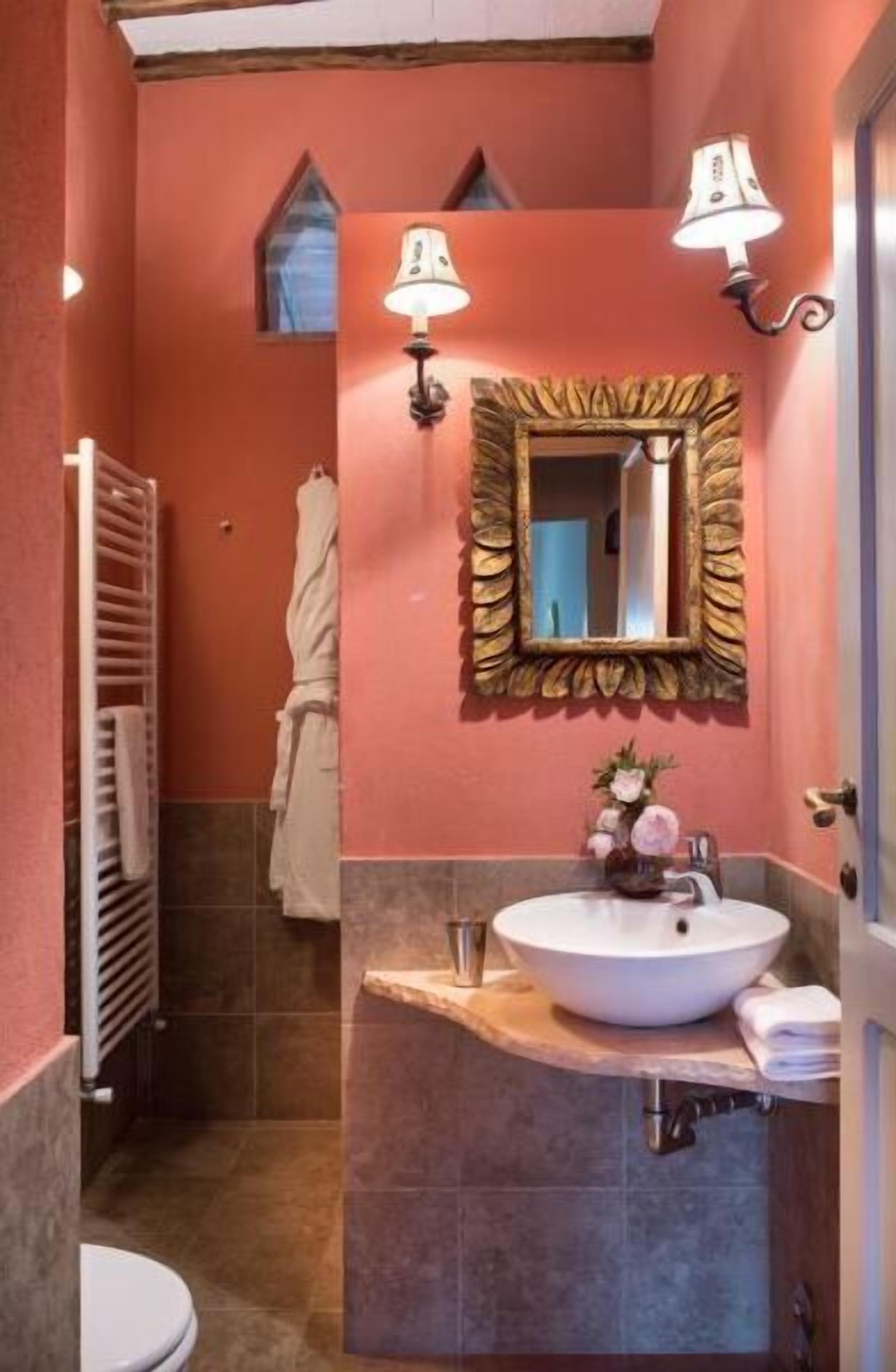 Un baño con un lavamanos blanco, un espejo con marco decorativo y dos lámparas de pared.