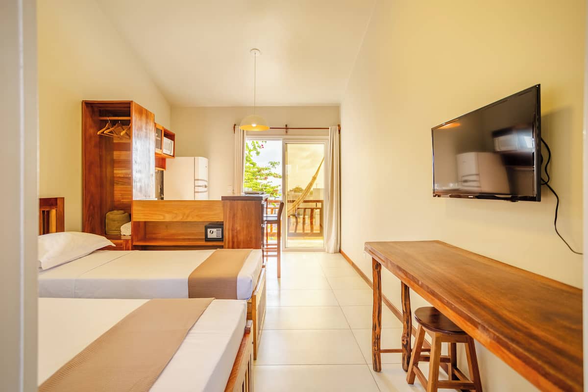 A hotel room with two beds, a wooden desk, a TV, and a wardrobe.