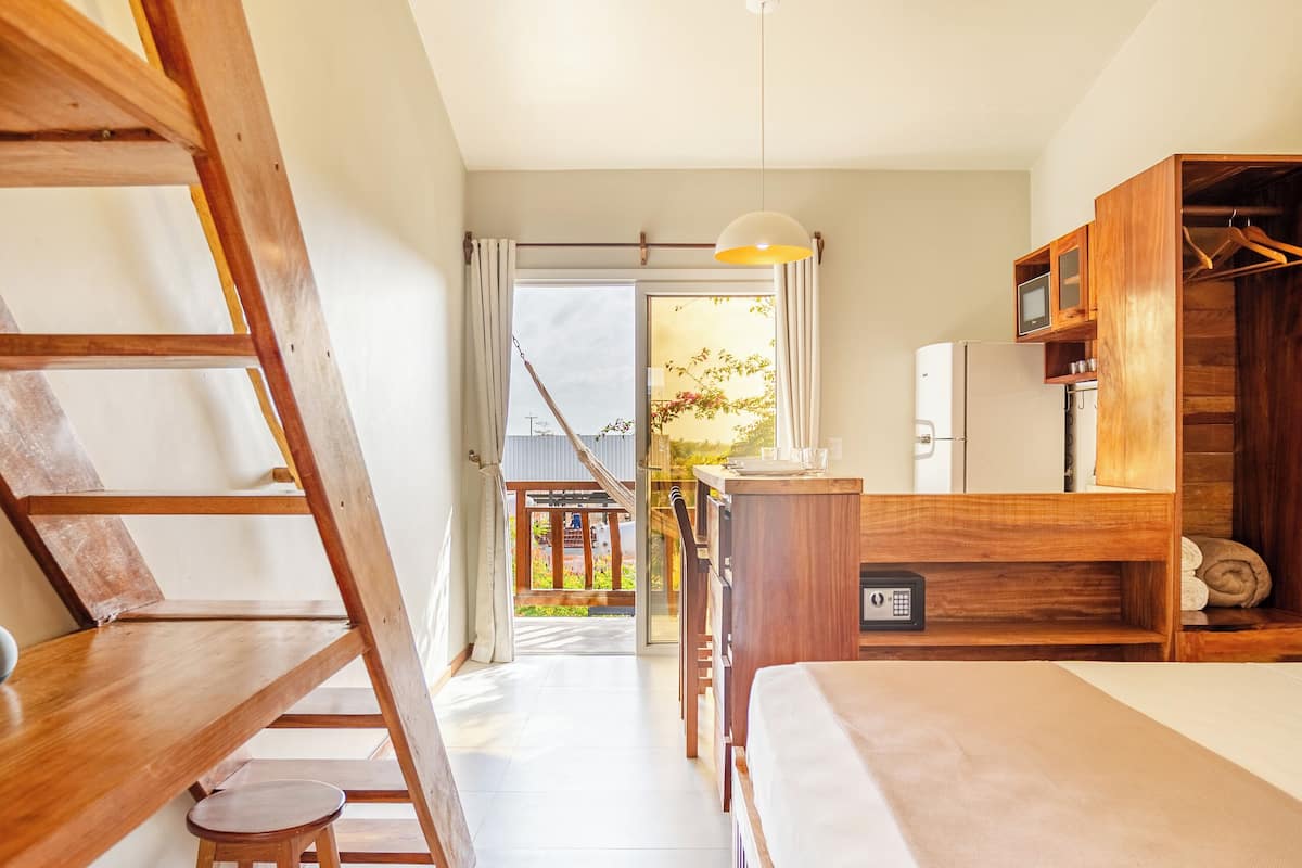 A bedroom with a wooden bed, a desk, and a chair. There is a wooden ladder and a window with curtains.