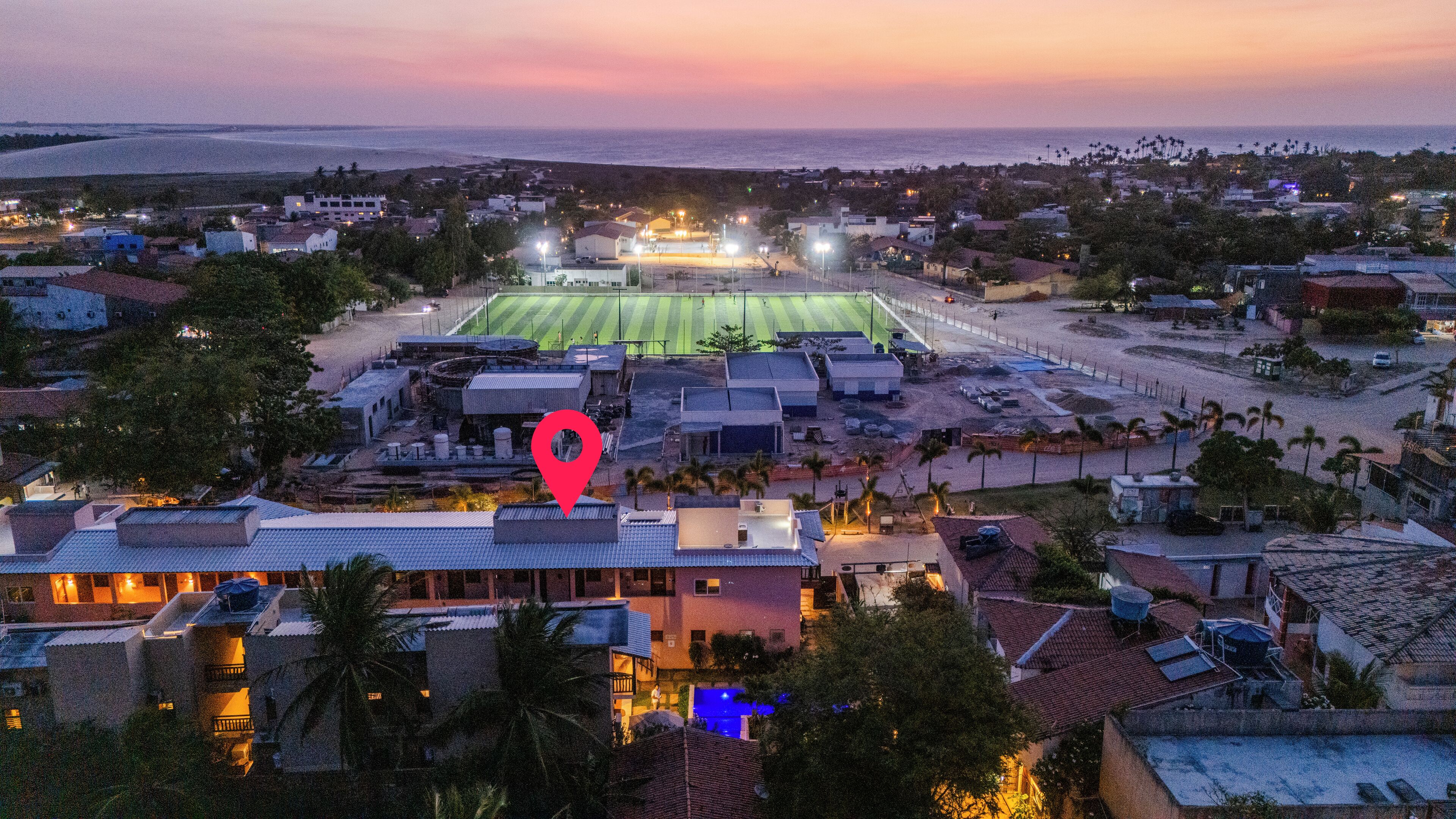 A stadium with a football field, surrounded by residential buildings and palm trees.