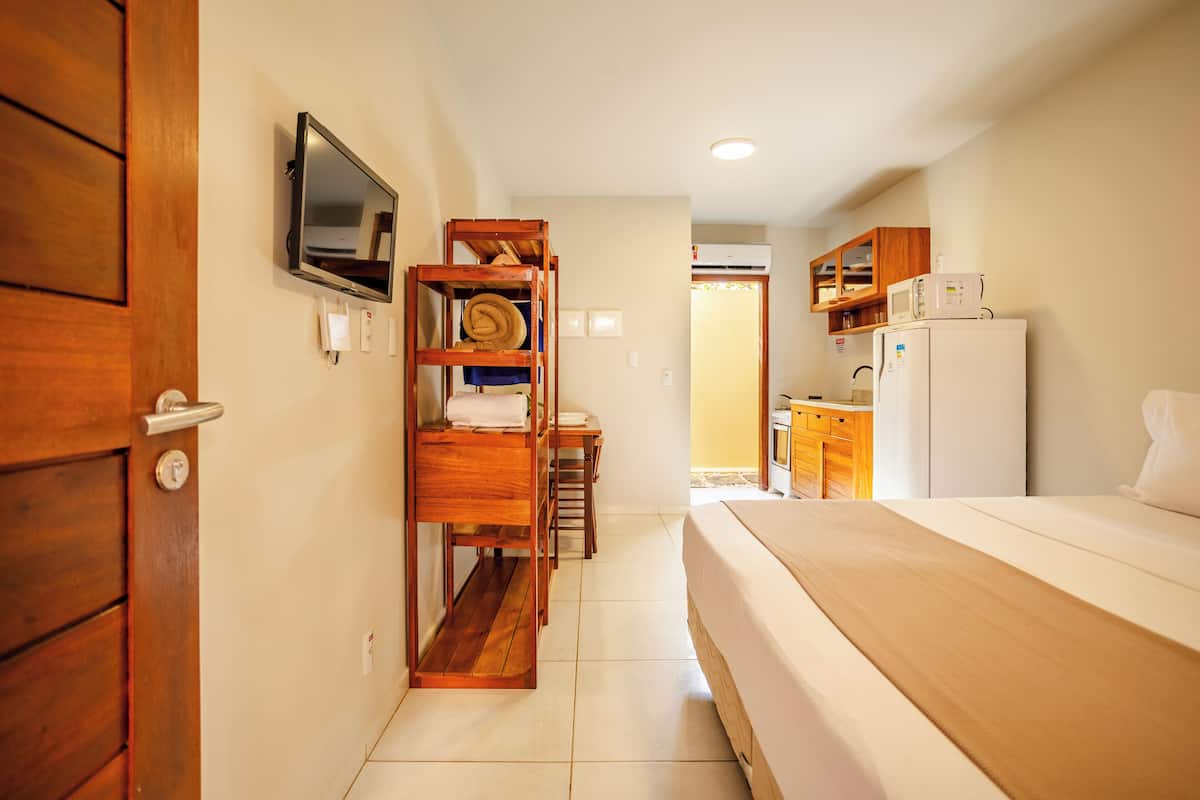 A hotel room with a bed, wooden furniture, a television, and a kitchenette.