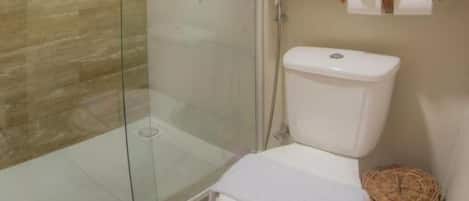 Un baño con ducha envuelta en vidrio, un inodoro blanco y una ventana de madera sobre el inodoro.