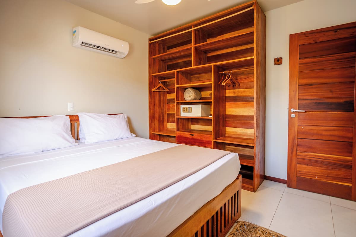 A bedroom with a large bed, wooden wardrobe, and an air conditioning unit on the wall.