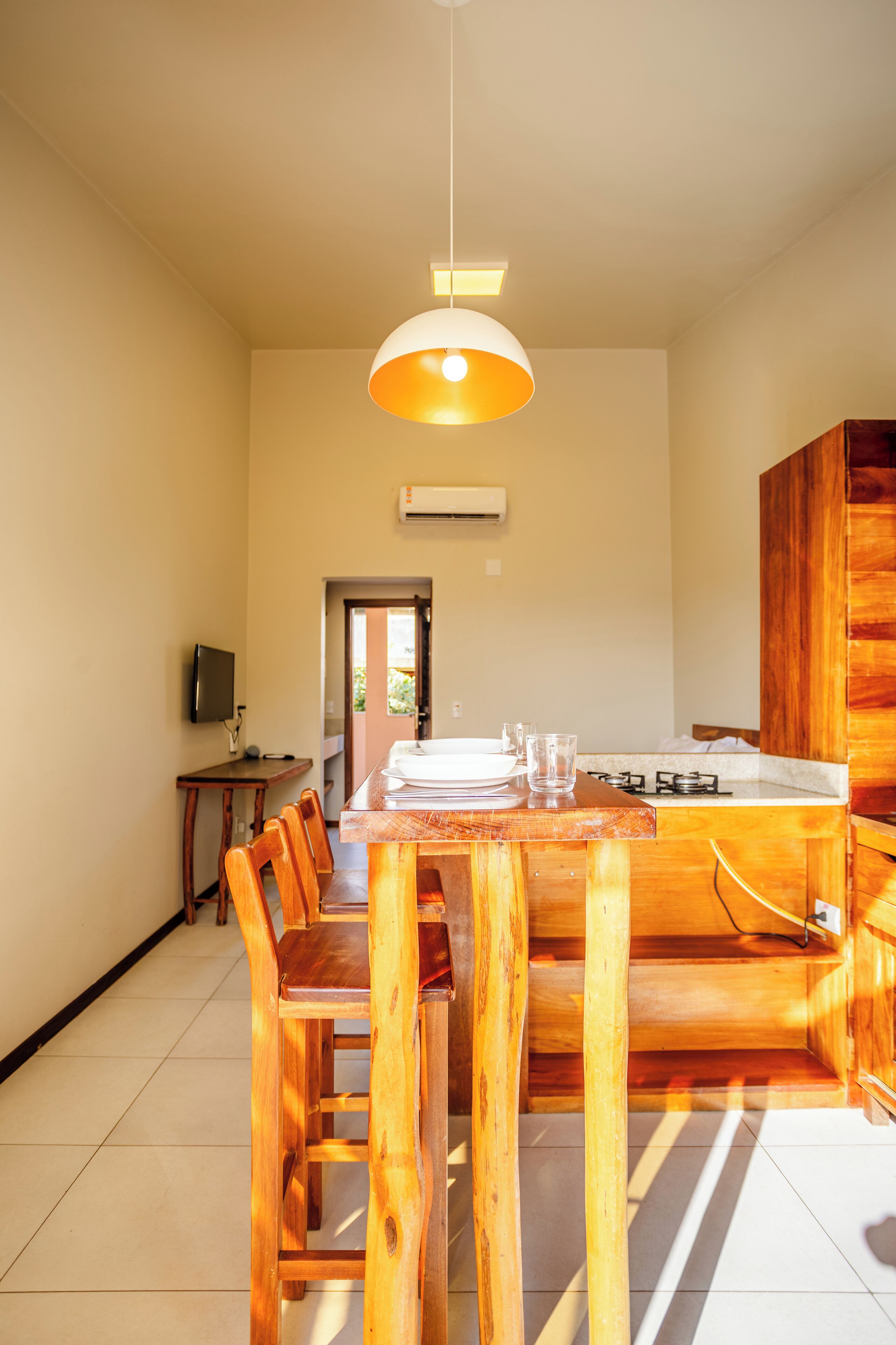 A dining area with a wooden table and chairs, a hanging light fixture, and a kitchen area with a stove.