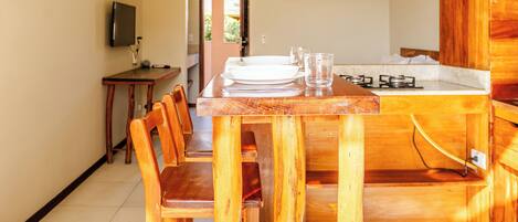 A dining area with a wooden table and chairs, a hanging light fixture, and a kitchen area with a stove.