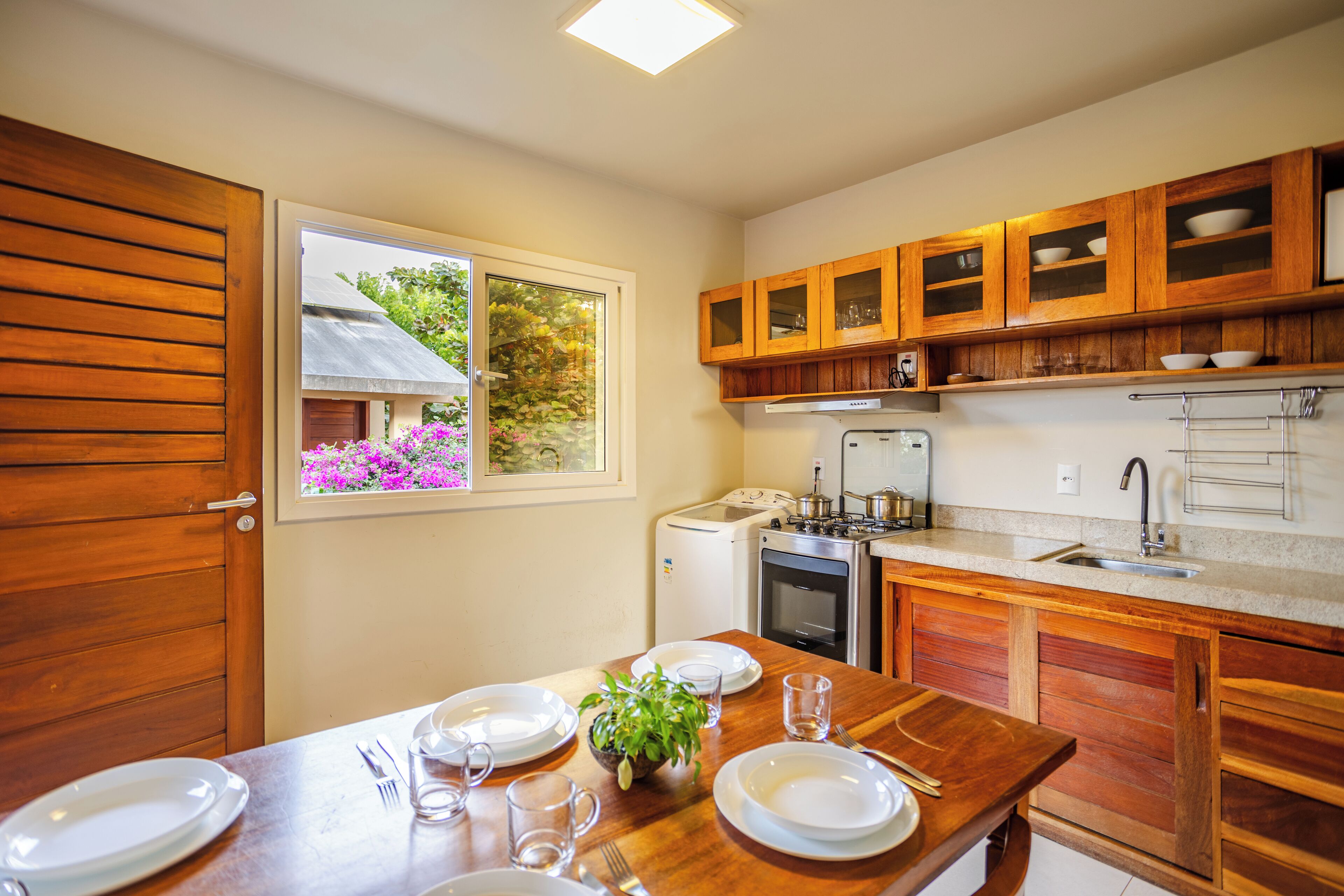 A modern kitchen with wooden cabinets, a built-in oven, and a window with a view of greenery.