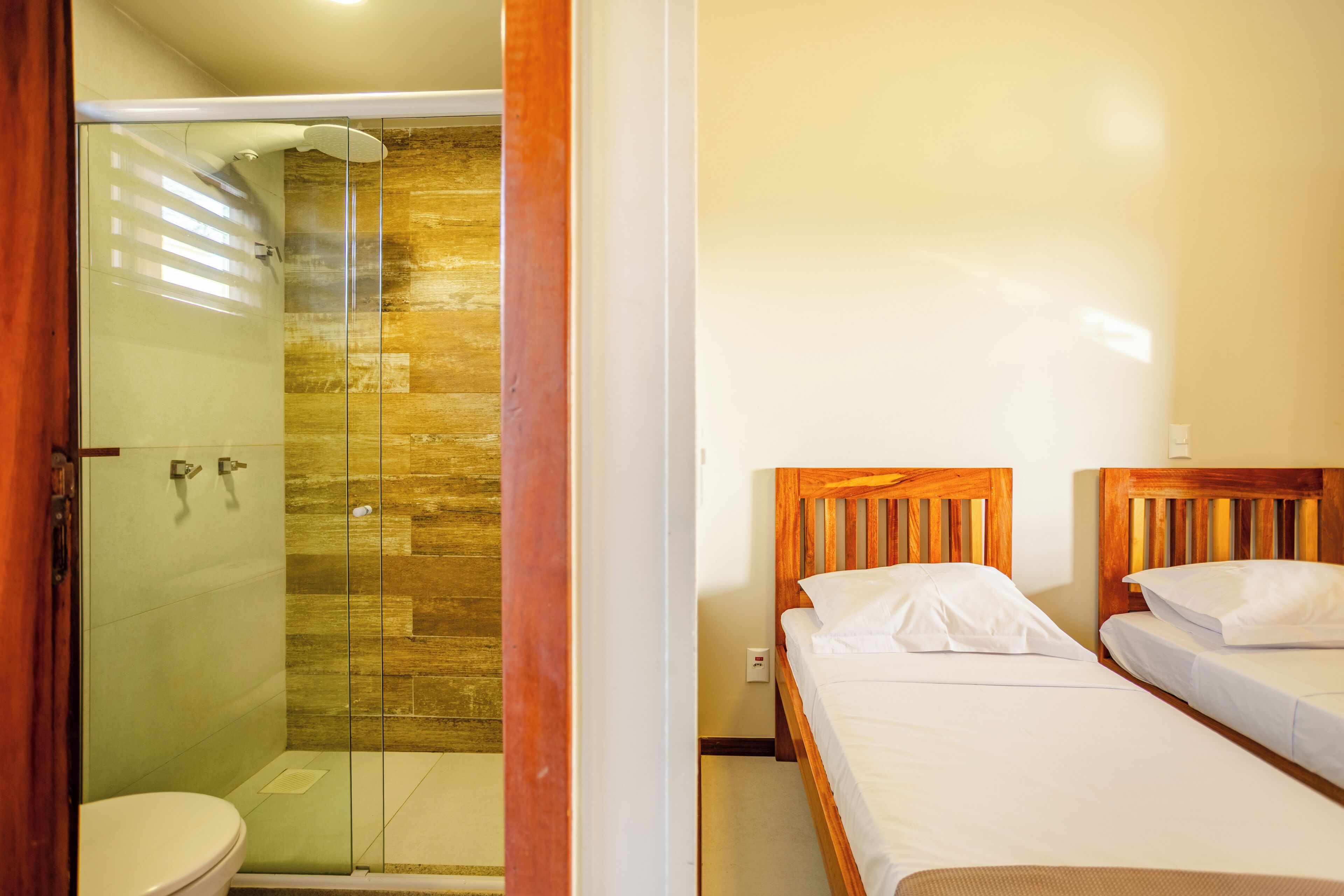 A bathroom with a glass-enclosed shower, a toilet, and two wooden beds with white bedding.