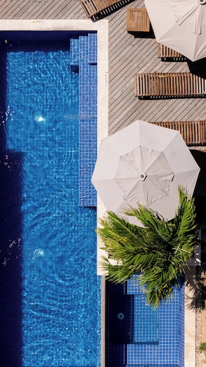 Vue aérienne d’une piscine aux parois carrelées, entourée d’une terrasse en bois et de chaises longues.