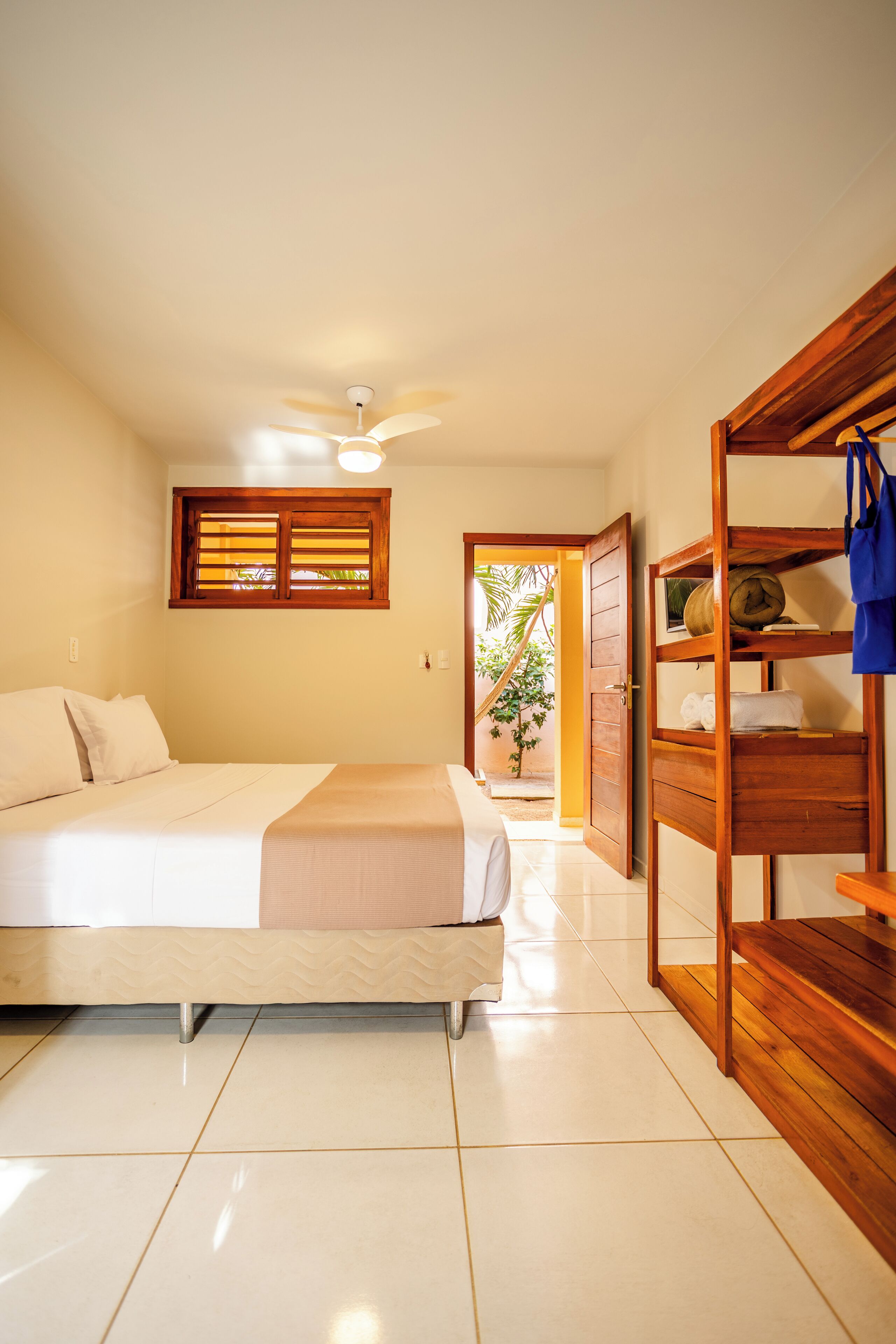 A bedroom with a bed, a ceiling fan, a wooden shelf, and a window with blinds.