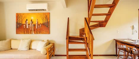 Un salon avec un canapé, une table à manger et des chaises, un escalier en bois et un tableau accroché au mur.
