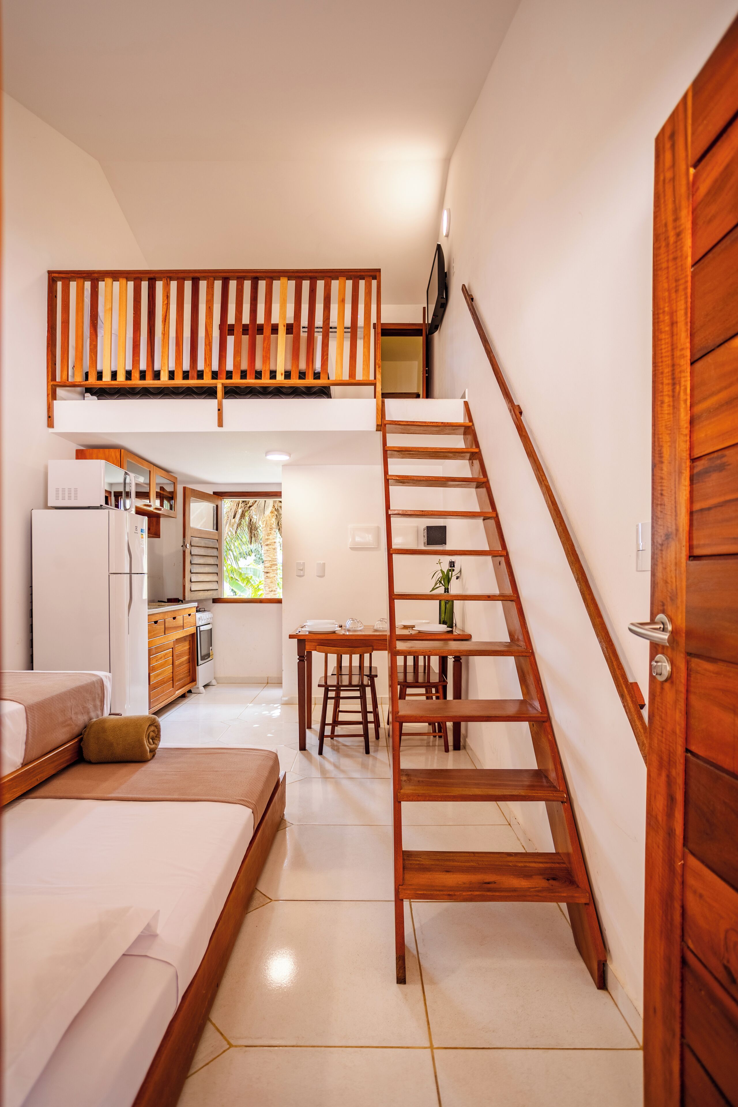 A compact hotel room with a bed, a kitchenette, a dining area, and a wooden staircase.