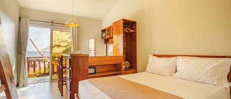 A hotel room with a bed, wooden furniture, a desk, and a view of the outside.