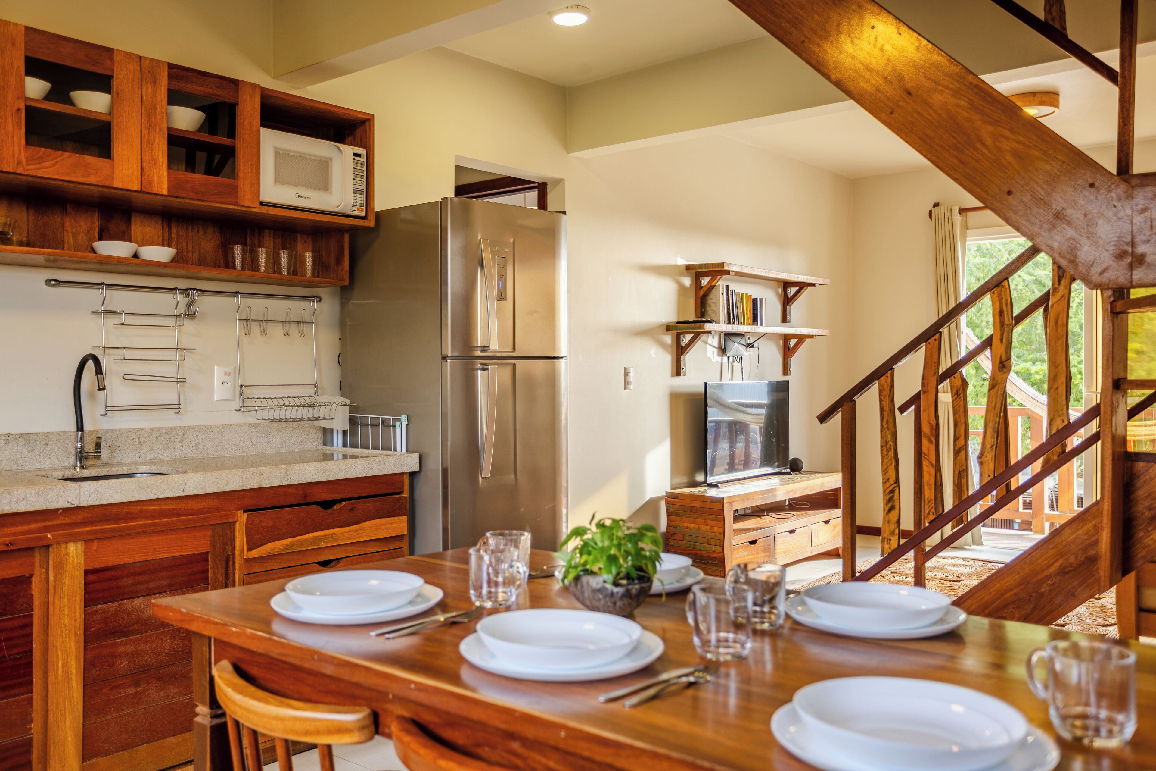 A modern kitchen with wooden cabinets, a stainless steel refrigerator, and a dining area set for four.