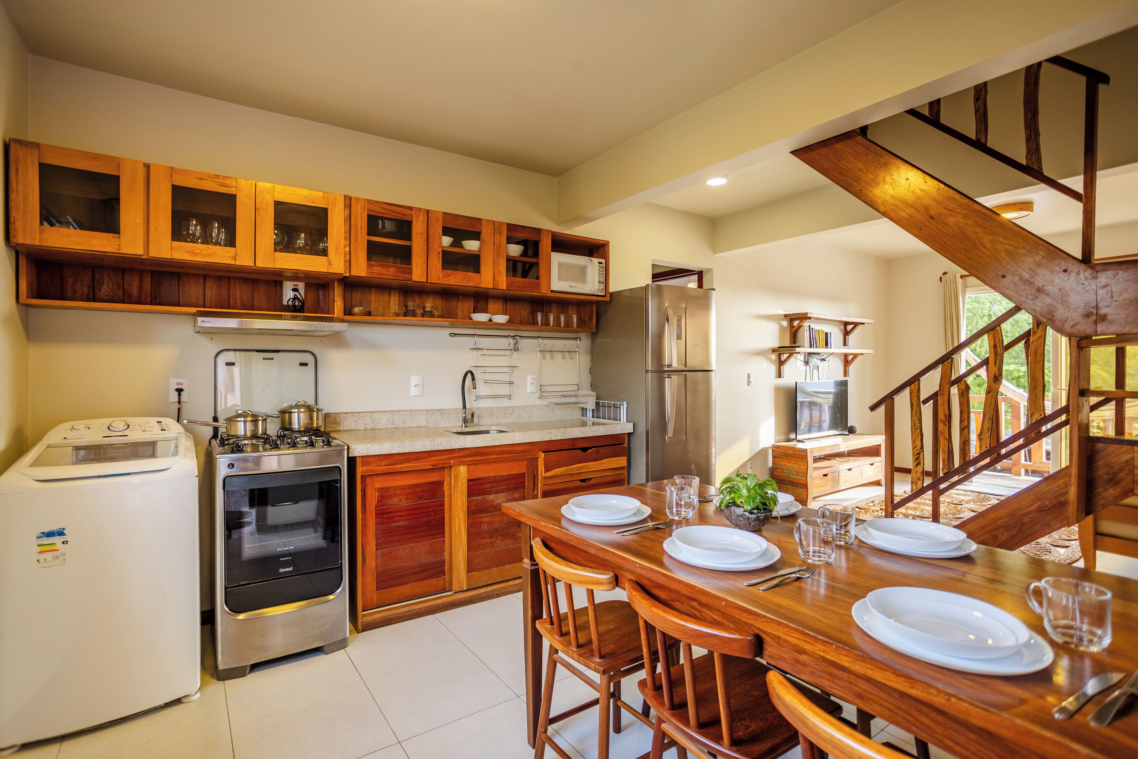 A kitchen with wooden cabinets, a stainless steel refrigerator, a stove, and a dining area with a table set for two.