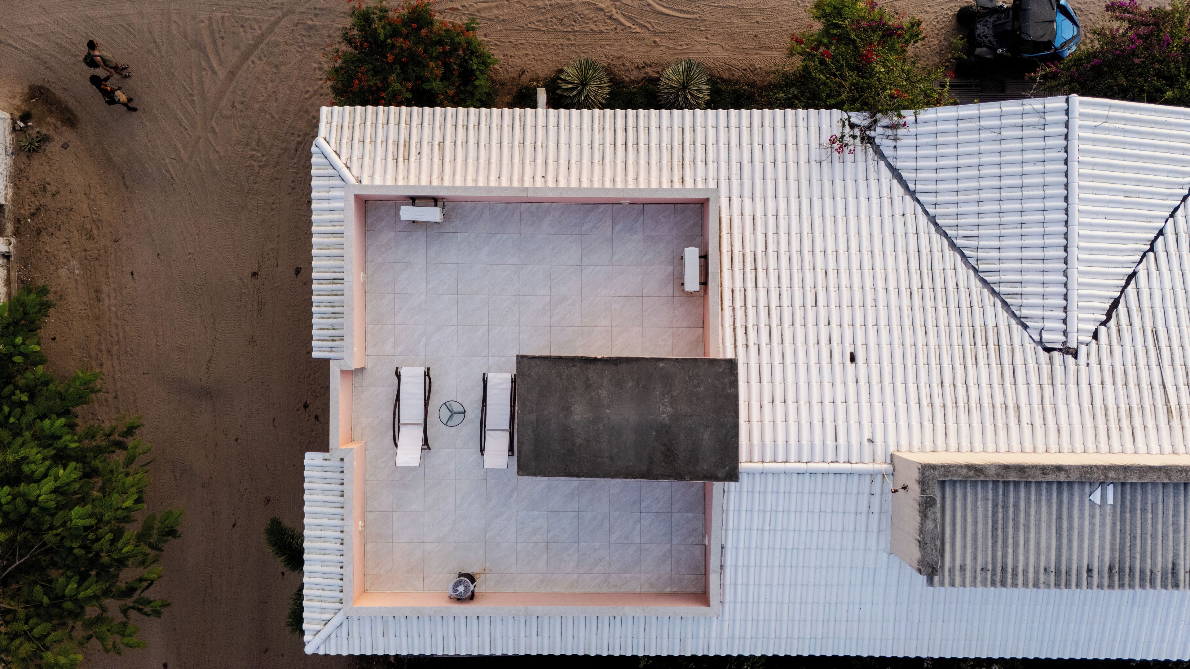 An aerial view of a modern building with a flat roof, a large open patio area with a table and chairs, and a small enclosed space with a fan.