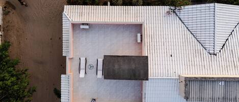An aerial view of a modern building with a flat roof, a large open patio area with a table and chairs, and a small enclosed space with a fan.