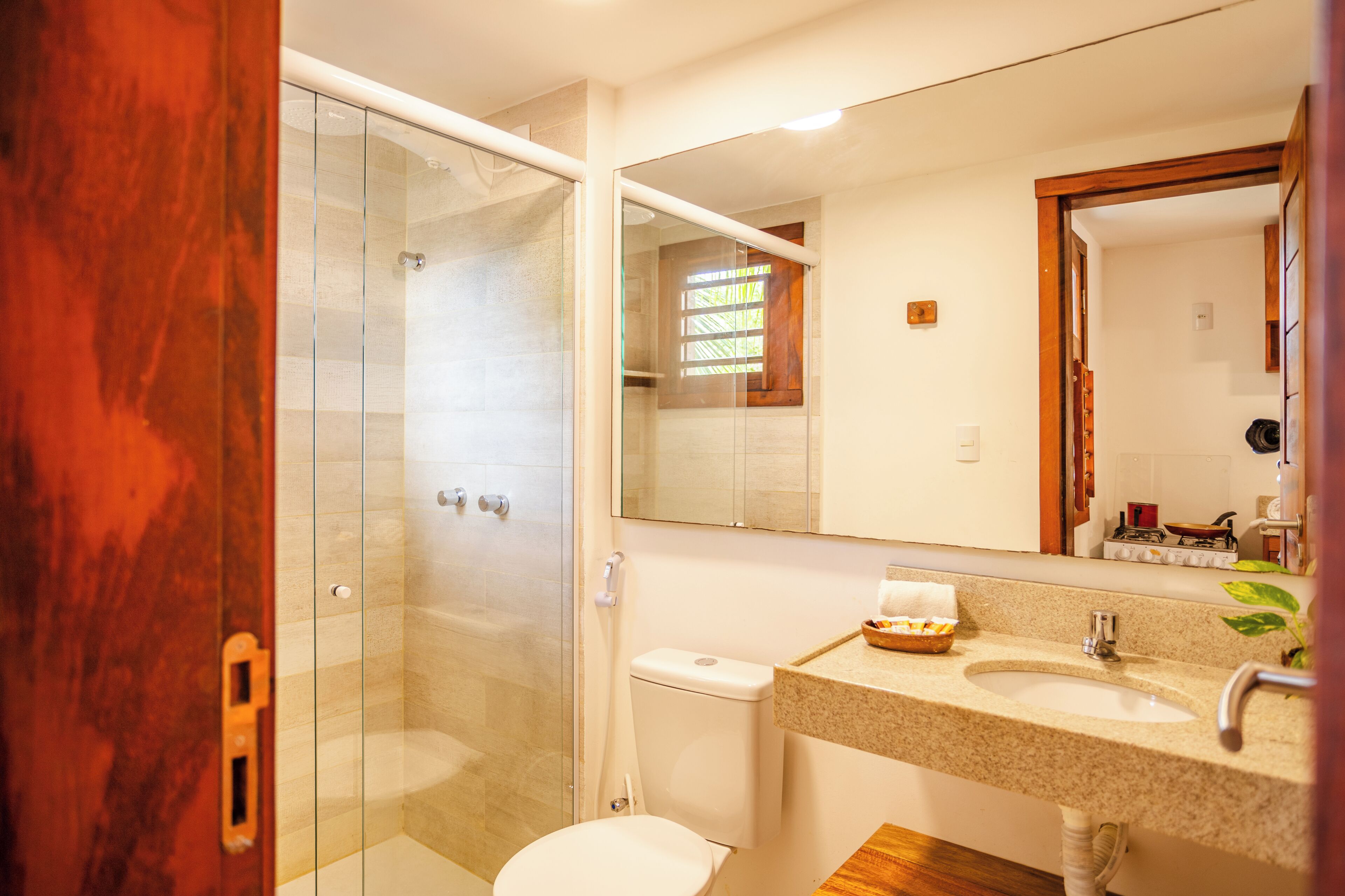Un baño con ducha envuelta en vidrio, un inodoro blanco, un lavamanos con espejo y piso de madera.